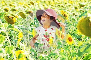 Cheerful girl in a wide-brimmed hat playing in the field with sunflowers