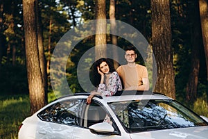 Cheerful girl woman and boy rejoices leaning out of the hatch of the car at a party in the summer in nature. The concept