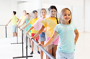 Cheerful girl working near ballet barre during group choreography class