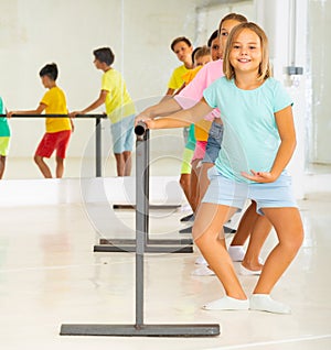 Cheerful girl working near ballet barre during group choreography class