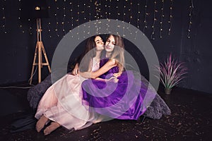 Cheerful girlfriends. Two long-haired girls in pink and purple dresses in studio on dark background with bokeh. Copy space.