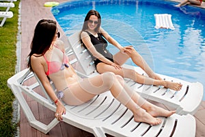 Cheerful girls telling jokes to each other while lying on the sunbeds