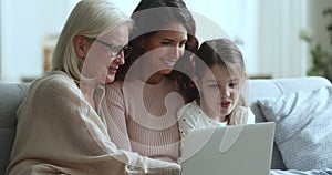 Cheerful girls and women of three family generations using laptop