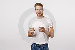 Cheerful good-looking modern blond man with bristle, holding paper cup of coffee, drinking tea and holding smartphone photo