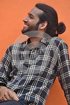 A cheerful good looking young man with beard and hair bun looking sideways while sitting outside