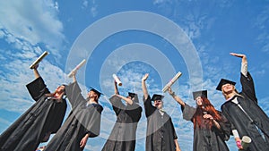 Cheerful graduates pose with raised diplomas on a sunny day.