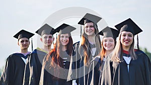 Cheerful graduates pose with raised diplomas on a sunny day.