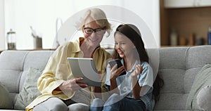 Cheerful grandmother and granddaughter child using wireless technology at home