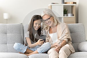 Cheerful granny and happy girl using application on mobile phone