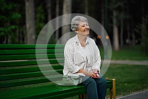 Cheerful granny leisures on bench in summer park