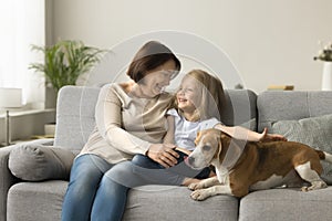 Cheerful granny and little granddaughter stroking cute dog, sitting close