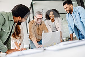 A cheerful group of diverse coworkers lean in around a laptop photo