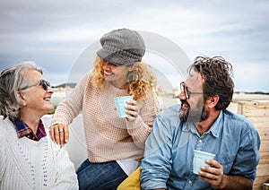 Cheerful group of family laughing together outdoor on terrace enjoying food and drink. Three people from senior to middle aged.