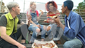 Cheerful group of teenagers enjoying rest eating pizza outdoors having fun