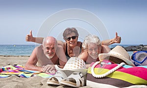 Cheerful group of three people friends mature and senior enjoying together holidays at the beach gesturing ok sign - active