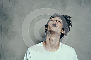 Cheerful guy with curly hair tilts his head to the side on a gray background photostudio model