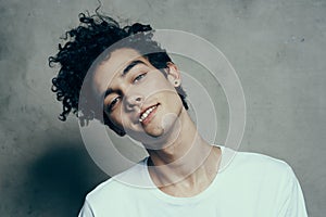 Cheerful guy with curly hair tilts his head to the side on a gray background photostudio model