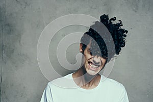 Cheerful guy with curly hair tilts his head to the side on a gray background photostudio model
