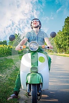 Cheerful guy fervently laughs riding a retro scooter