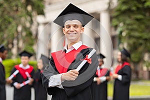 Cheerful guy in graduation costume with diploma posing outdoors