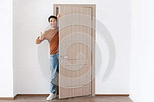 Cheerful guy looking out of door showing thumb up gesture