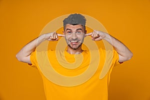 Cheerful guy plugging his ears isolated over yellow background