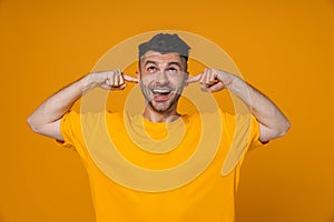 Cheerful guy plugging his ears isolated over yellow background