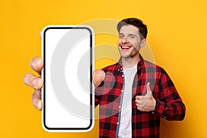 Cheerful guy showing big white empty smartphone screen and like