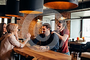 Cheerful gyu and girl having fun arm wrestling each other in pub.