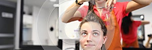 Cheerful hairdresser in apron hold bunch of hair for client and cut off with scissors.