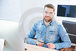 Cheerful handsome designer holding stylus and sitting in office