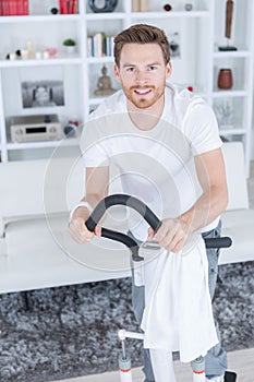 Cheerful handsome male exercising on apartment bicycle