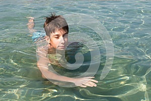 Cheerful handsome teen boy swiming in turquoise blue sea water above water surface and underwater. Beach, summer vacation, teenage