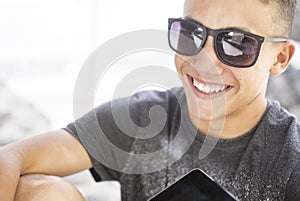 Cheerful handsome teenage boy smiling in modern sunglasses with digital tablet. Happy male teenager having fun spending leisure