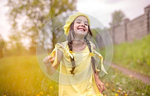 Cheerful and happy charming little girl in a yellow knitted beret and a yellow dress, dancing in nature in the spring