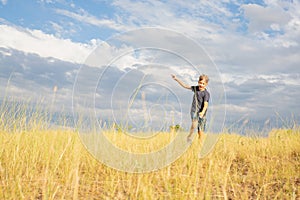 A cheerful, happy child runs through a summer field with yellow grasses against a blue cloudy sky.