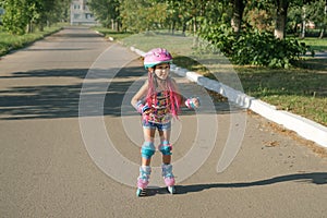 A cheerful happy child in a sports protective helmet and knee pads is skating on an asphalt path in the suburbs.