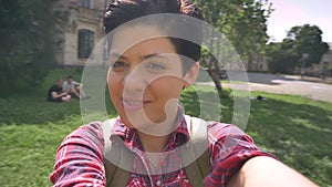 Cheerful happy college student recording video with selfie camera and turning around, smiling and laughing in park near