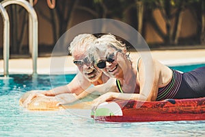 Cheerful happy coule of retired senior old people smile and enjoy together the pool in summer hoiday vacation with coloure trendy