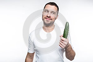 Cheerful and happy guy is holding a big and long cucumber. He likes to eat organic and natural food. This man is a vegan