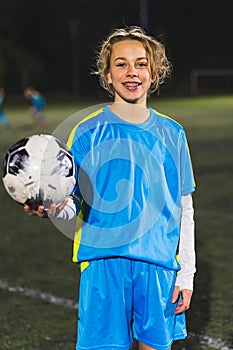 cheerful and happy little girl in a blue uniform holding a soccer ball and taking a photo