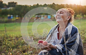 Cheerful happy mature senior woman holding red apples sitting in her garden