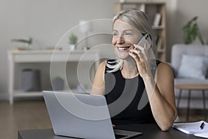 Cheerful happy middle aged entrepreneur woman talking on cellphone