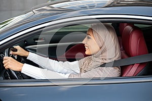 Cheerful happy muslim woman in hijab driving her new car