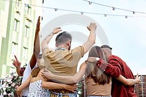 Cheerful happy people having party outdoors, raising hand up celebrating, view from back