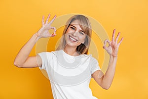 Cheerful happy pleased young pretty blonde woman posing isolated over yellow wall background dressed in white casual t-shirt