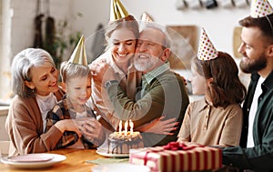 Cheerful happy senior man hugging with daughter while celebrating his birthday with big loving family