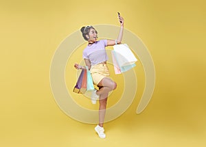 Cheerful happy teen asian woman enjoying shopping, she is carrying shopping bags and smartphone to get the latest offers at the