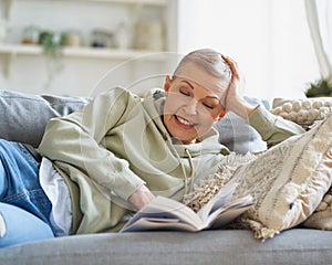 Cheerful happy woman reading book and smiling while relaxing on sofa at home