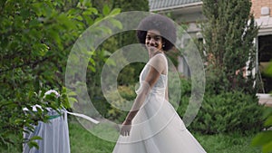 Cheerful happy young African American woman in wedding dress spinning looking at camera. Portrait of excited joyful